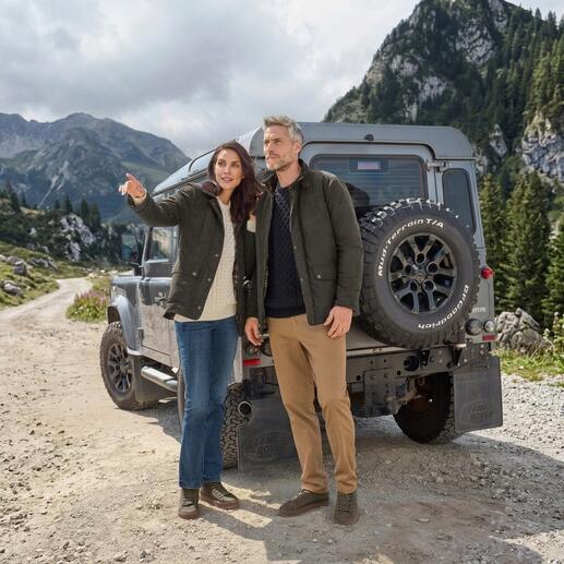Couple en vestes d'extérieur se tient devant un véhicule tout-terrain dans un environnement naturel.
