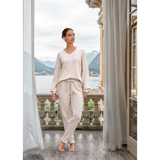 Femme en pull beige se tenant sur un balcon avec vue sur les montagnes.