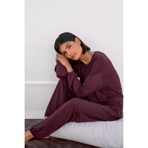 Femme assise sur un coussin portant un haut et un pantalon de loungewear mauve.