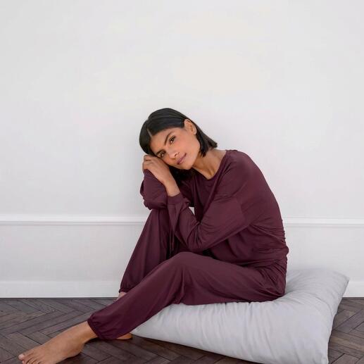 Femme assise sur un coussin portant un haut et un pantalon de loungewear mauve.
