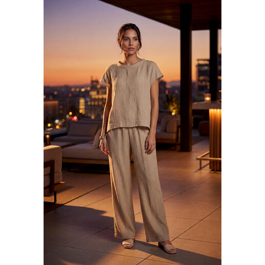 Femme portant une blouse couleur sable et un pantalon large sous la lumière du soir.