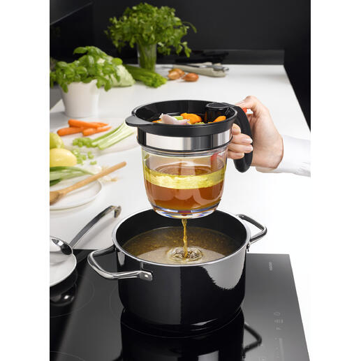 Main utilisant un tamis pour verser du bouillon de légumes dans une casserole, avec une cuisine en arrière-plan.