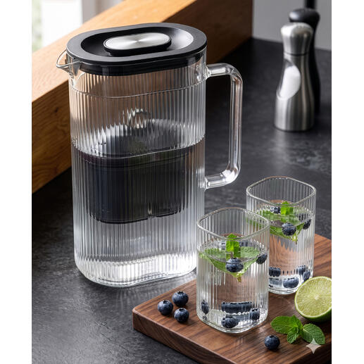 Carafe filtrante avec un verre supplémentaire et des herbes fraîches.