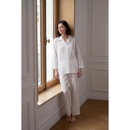 Femme en pyjama rayée en coton soie se tient élégamment devant la fenêtre