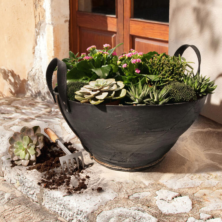 Panier en pneus de camion avec des plantes colorées, décoratif et durable sur une surface en pierre.