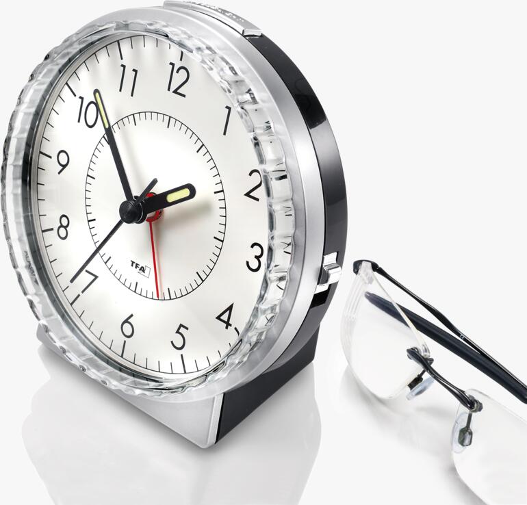 Réveil analogique avec boîtier noir et aiguilles rouges à côté de lunettes.