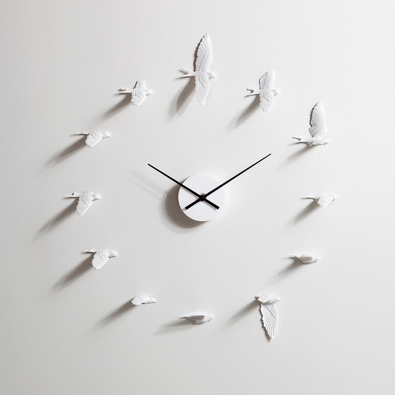 Horloge murale moderne en forme d'hirondelles, aiguilles noires sur fond clair.