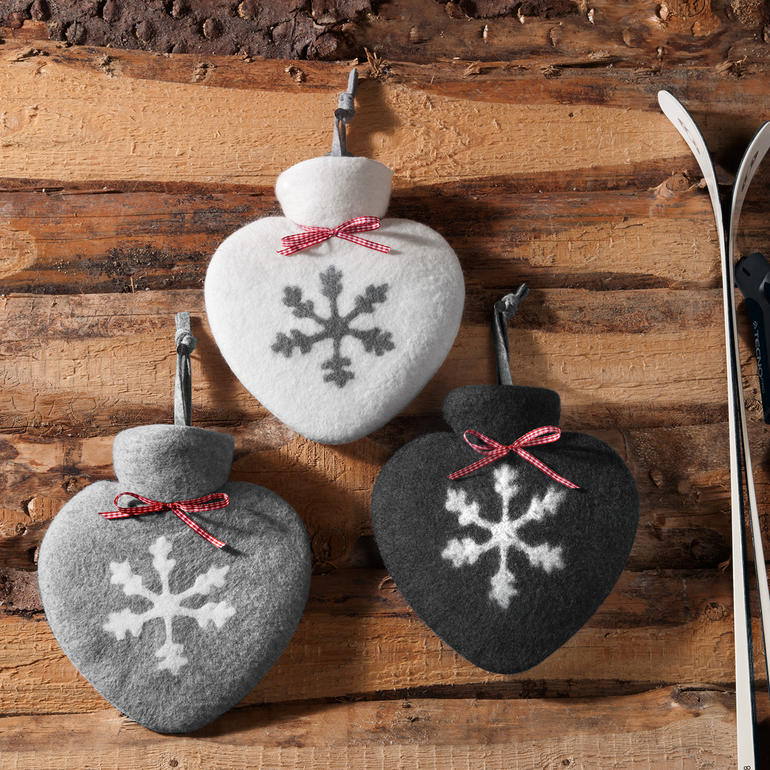 Trois bouteilles d'eau chaude feutrées à la main en forme de cœur avec des motifs de flocons de neige.