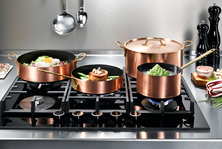 Casseroles en cuivre à induction sur une cuisinière avec plusieurs casseroles et une poêle.