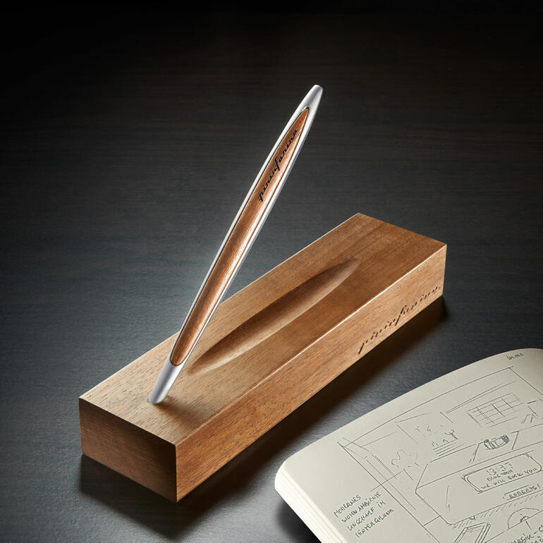Stylé stylo Pininfarina Ethergraf® sur un bloc en bois à côté d'un carnet de croquis.