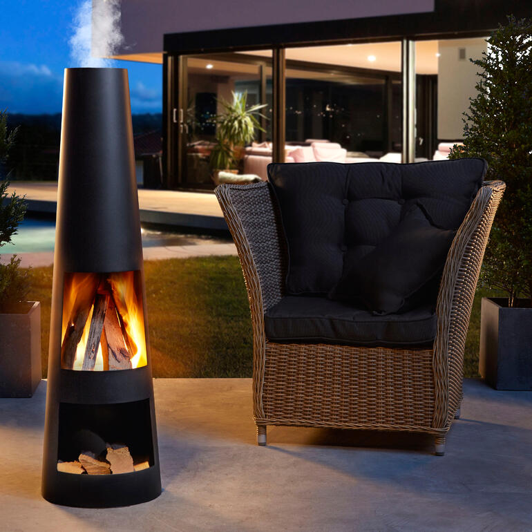 Moderne cheminée de terrasse avec du bois brûlant à côté d'un fauteuil confortable.