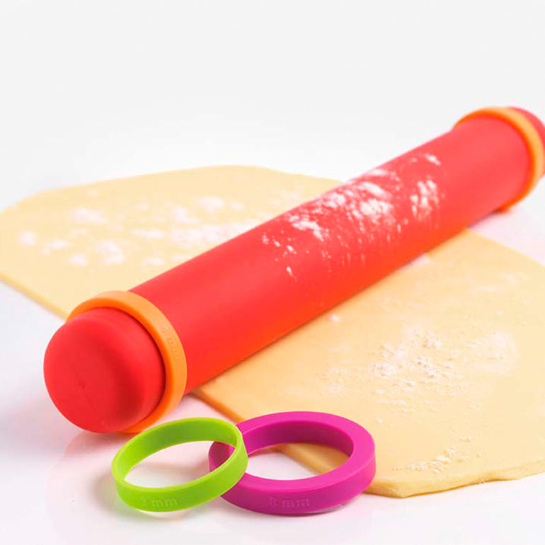Rouleau à pâtisserie Vario en silicone rouge avec anneaux amovibles sur une feuille de pâte.