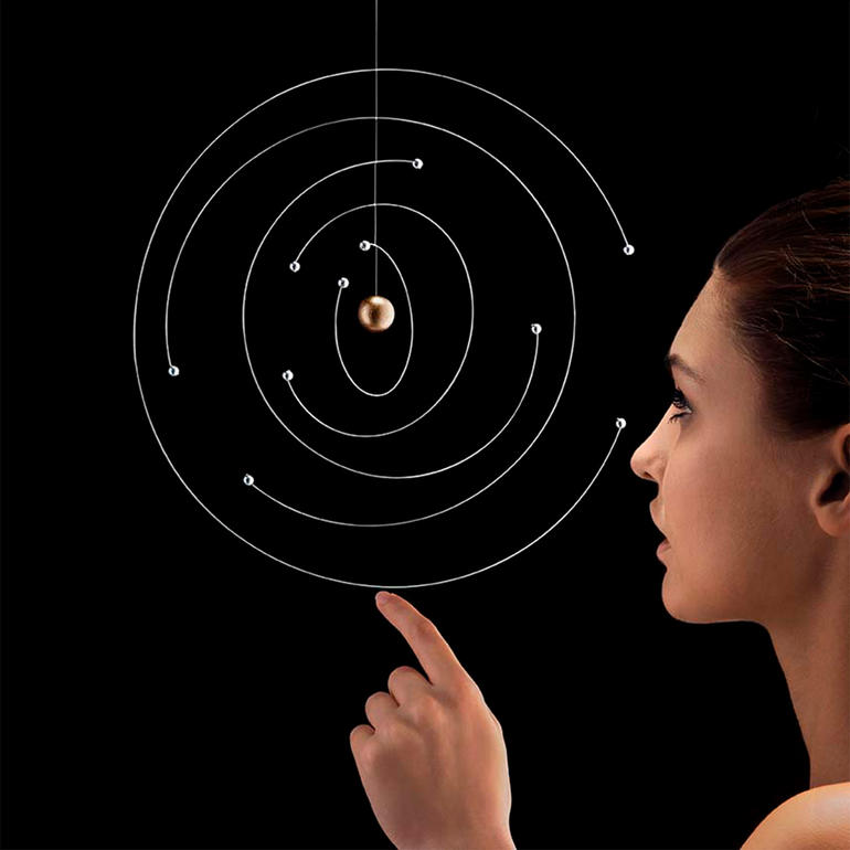 Femme montrant un modèle atomique flottant avec des billes et des trajectoires en spirale.