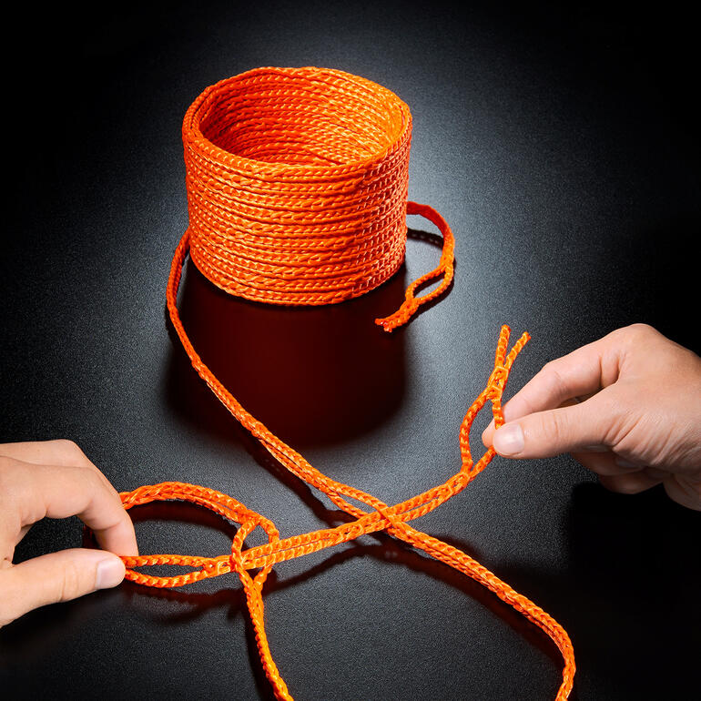 Corde à boucle orange sur fond noir, une main faisant un nœud.