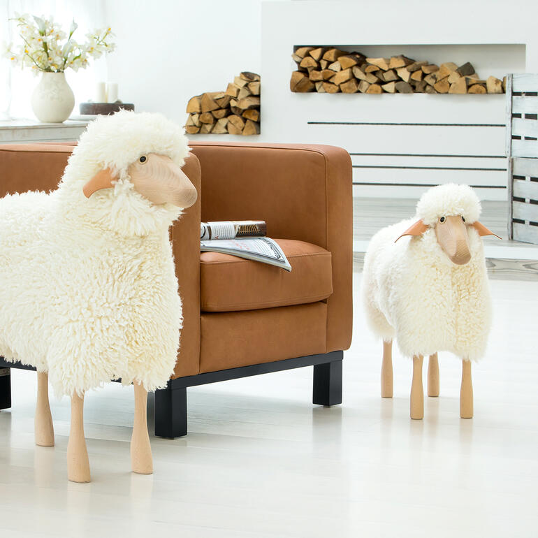 Deux moutons grandeur nature en peluche dans un salon devant un canapé.
