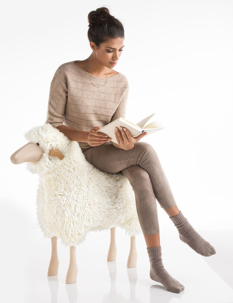 La structure en bois massif est ultra résistante, afin que vous puissiez utiliser cet objet design en tant que tabouret. Femme assise sur un mouton en train de lire un livre.