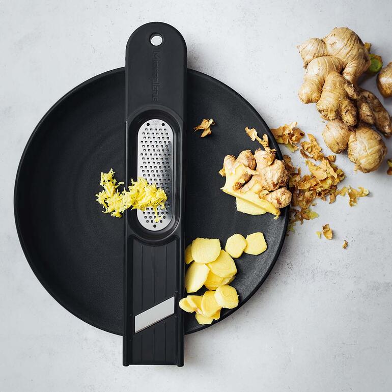 Râpe à gingembre 3-en-1 sur une assiette avec du gingembre frais.