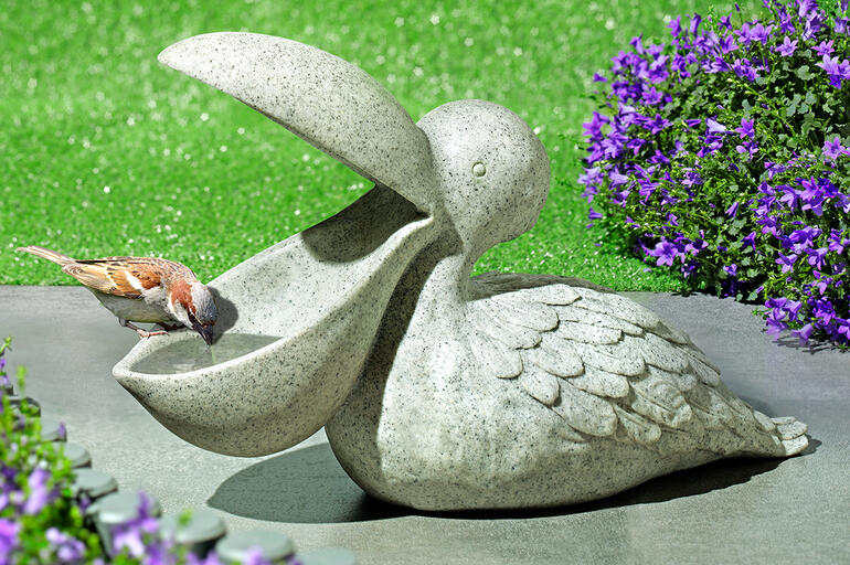 Abreuvoir à oiseaux en forme de pélican en pierre sur du gazon vert.