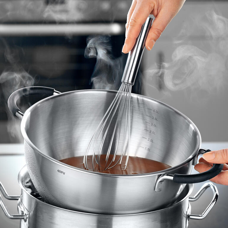 Placé sur un bain-marie, le bol est très pratique pour faire fondre du chocolat. Main tenant un fouet dans un bol en train de cuire à la vapeur au bain-marie.