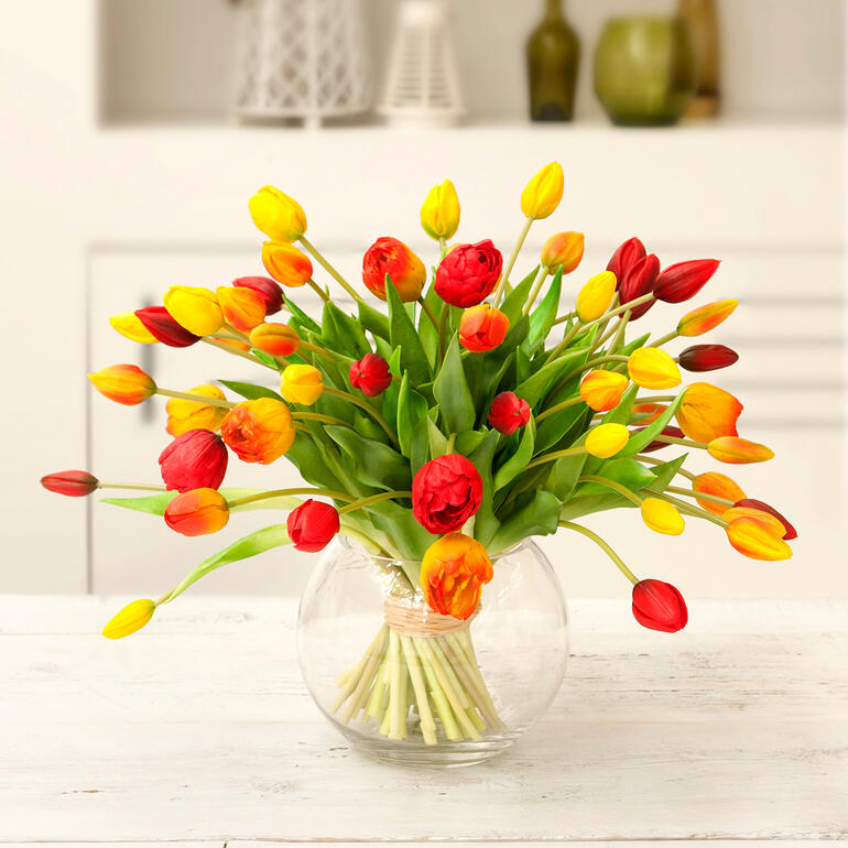 Jaune/Orange/Rouge Bouquet de tulipes colorées dans un vase en verre rond.