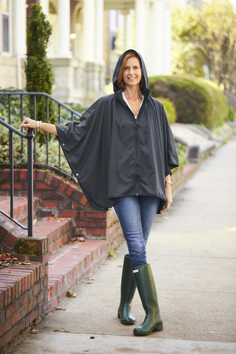 Femme portant un poncho de pluie noir de style sportif avec capuche, debout à l'extérieur.