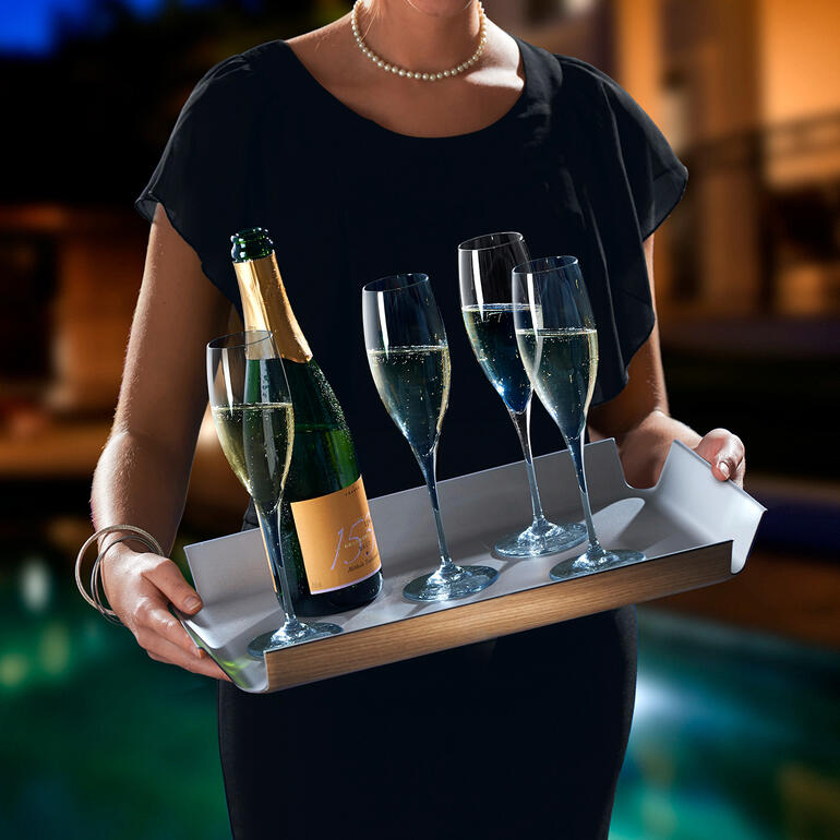 Plateau antidérapant au design en bois tenu par une femme avec du champagne et des verres.