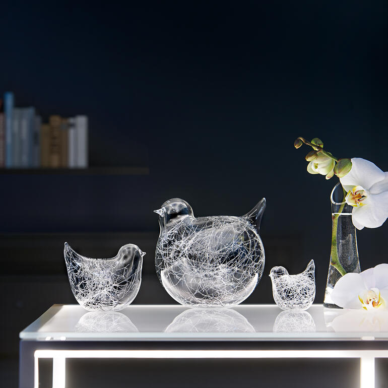 Ensemble de trois oiseaux en verre décoratifs sur une table, entourés de plantes.