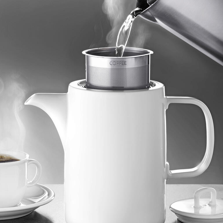 Cafetière blanche avec filtre, l'eau y coule.