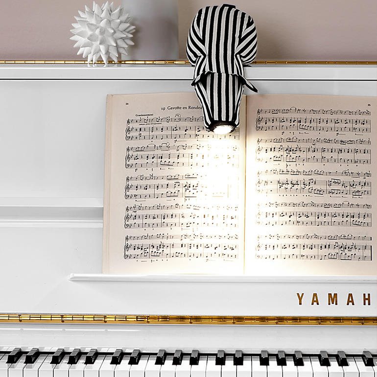 Lampe de lecture en forme de chien rayé éclairant une partition sur un piano.