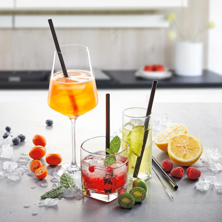 Trois boissons avec des pailles en verre et des fruits décorant une surface de table.