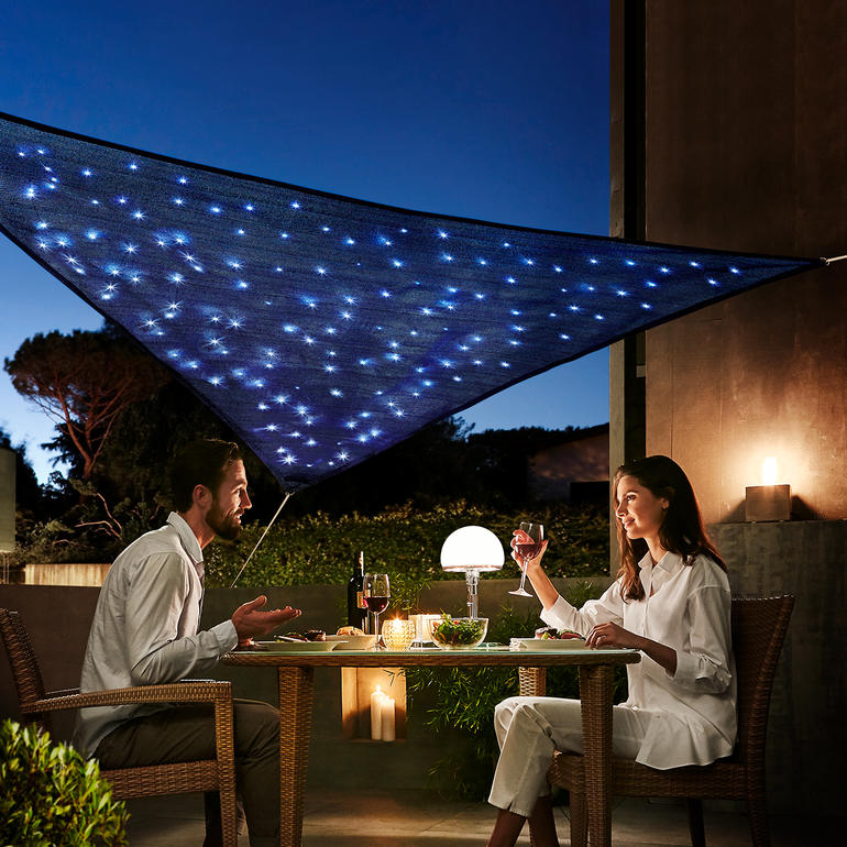 Un couple utilise un voile d'ombre 'Ciel étoilé' lors d'un dîner en extérieur.