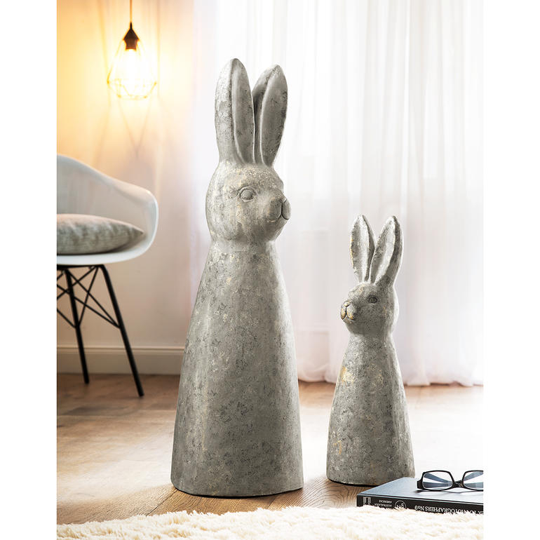 Statue de lapin en béton à côté d'une plante à l'intérieur.