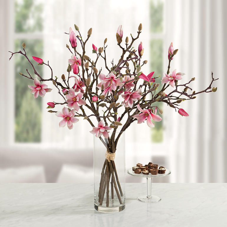 Branche de magnolia avec des fleurs roses dans un vase en verre sur un fond clair.
