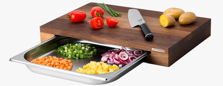 Planche à découper professionnelle en bois avec bac de récupération et légumes colorés.