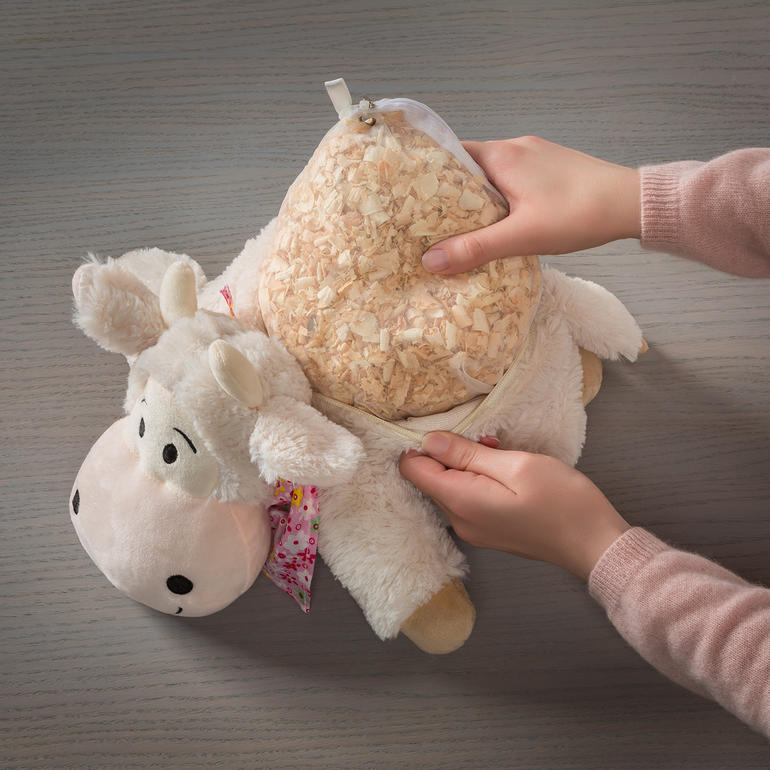 Mains ajoutant des copeaux de bois de cèdre dans l'ouverture d'une peluche de vache