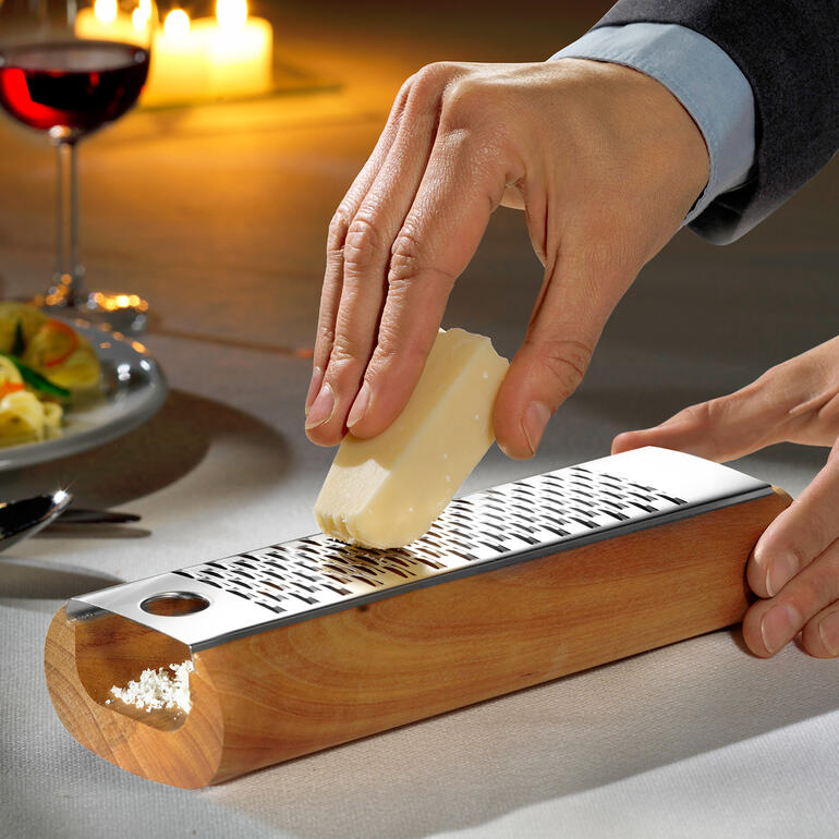 Homme râpe du fromage sur une râpe à fromage en bois au design.