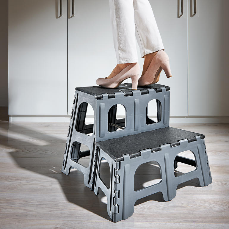 Une personne se tient sur un escabeau pliable à deux niveaux dans une cuisine moderne.