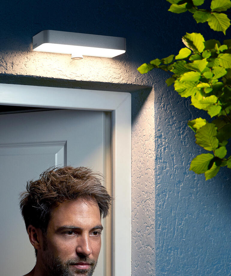 Homme se tenant sous une applique extérieure près de la porte.