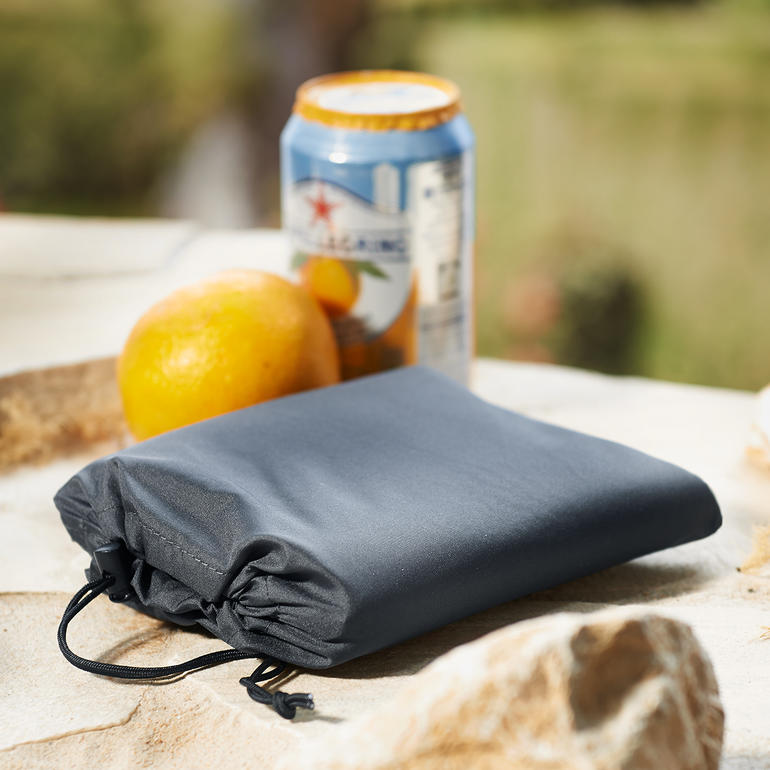 Transport facile en le repliant et en le mettant dans la pochette fournie. SoftAirSeat compact roulé à côté d'une canette et d'une orange.