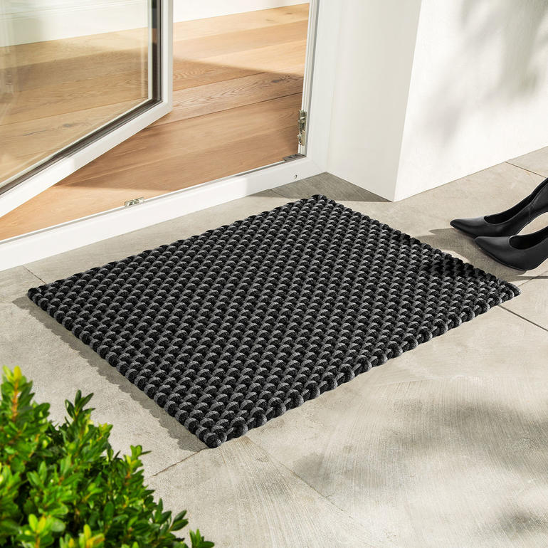 Tapis cordé noir/gris devant une porte sur le sol.