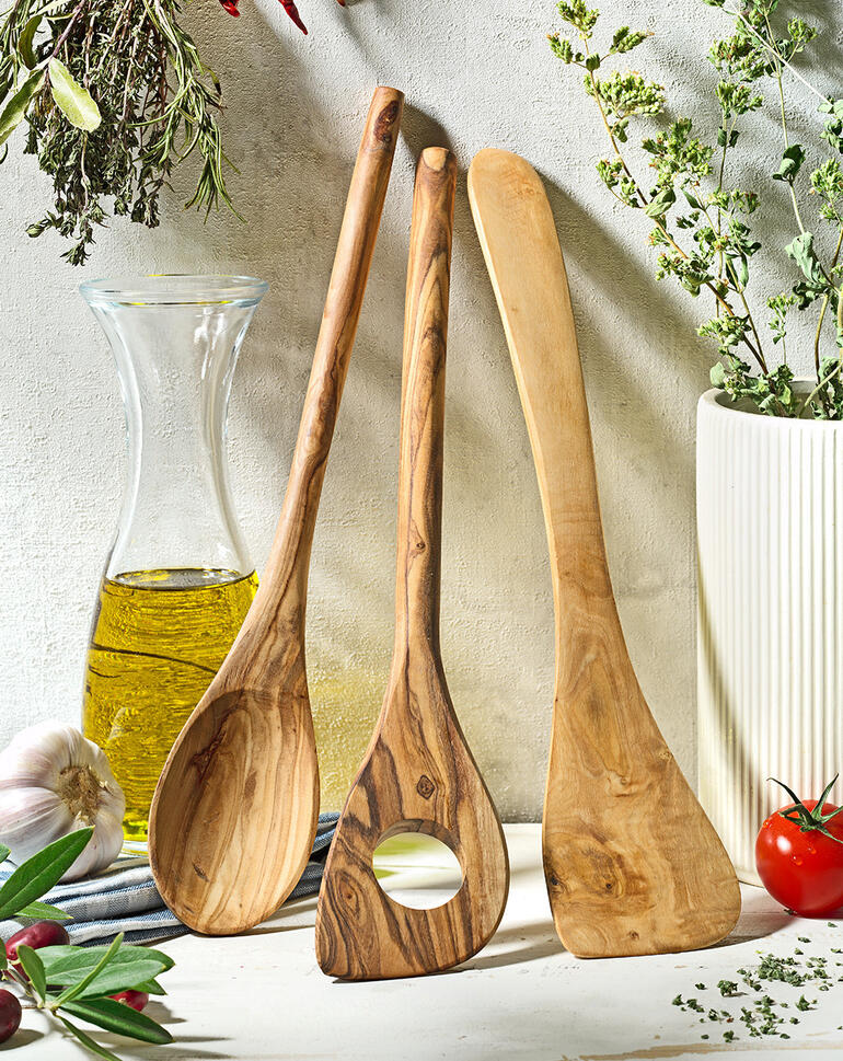 Ustensiles de cuisine en bois d'olive de trois pièces sur une table rustique avec des herbes.