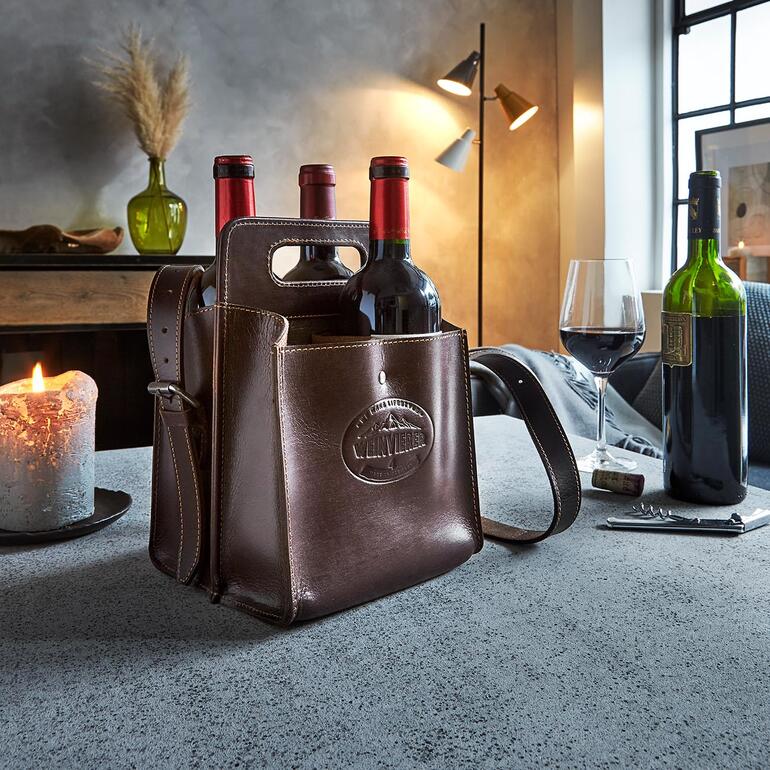 Le modèle « Weintragerl » contient 4 bouteilles de 0,7 l. Porte-bouteilles en cuir de buffle avec des bouteilles de vin, sur une table dans une pièce élégante