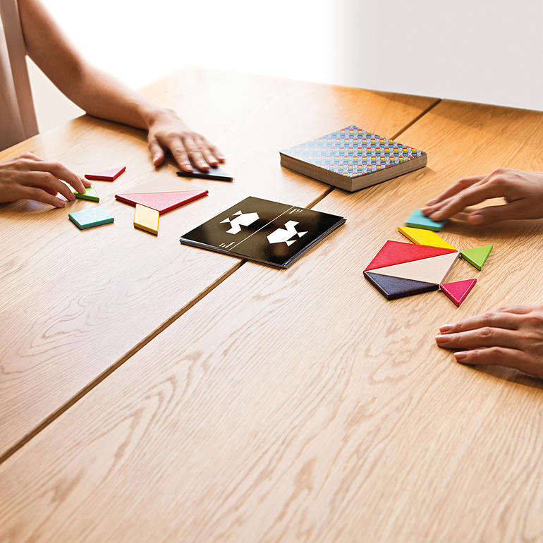 Deux personnes jouent au Tangram sur une table en bois.