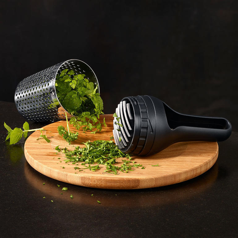 Hachoir intégré pour hacher finement vos aromates. Presse à herbes Rösle avec des herbes fraîches sur une planche en bois.