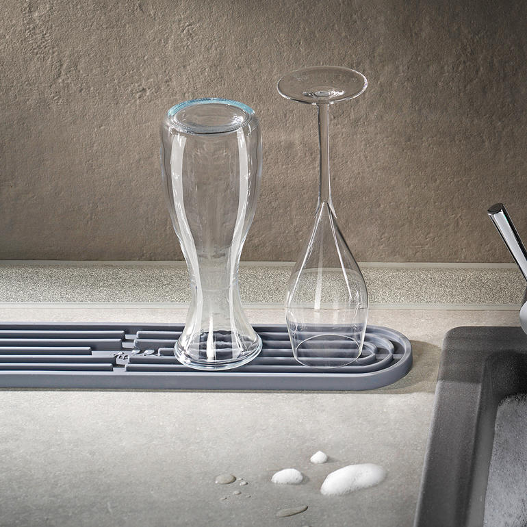 Des verres sèchent sur un tapis de séchage gris.