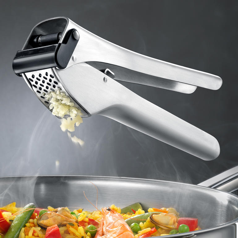 Presse-ail en acier inoxydable au-dessus d'une poêle avec des légumes colorés