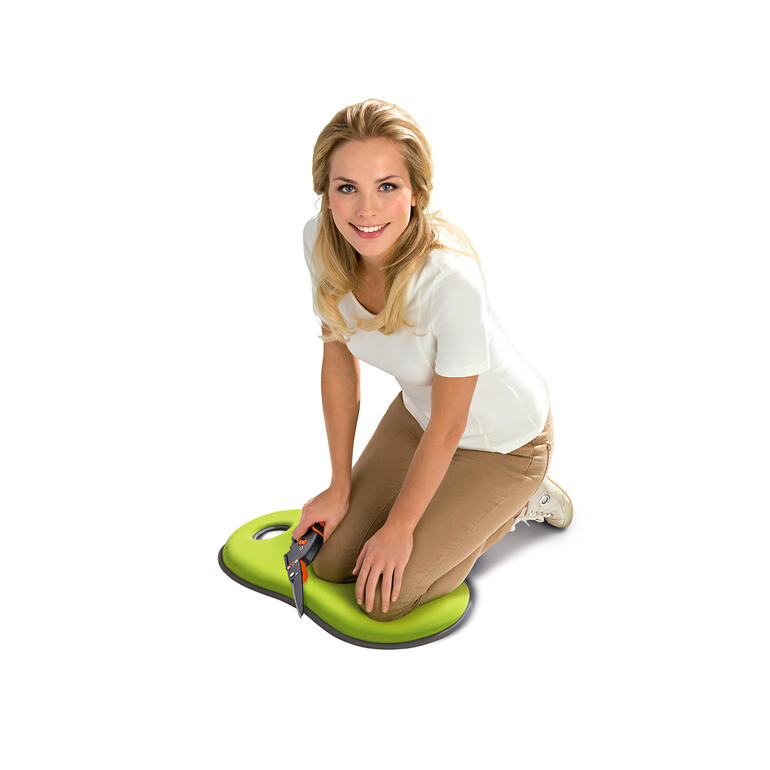 Femme à genoux sur un coussin vert pour genoux et assise dans le jardin.