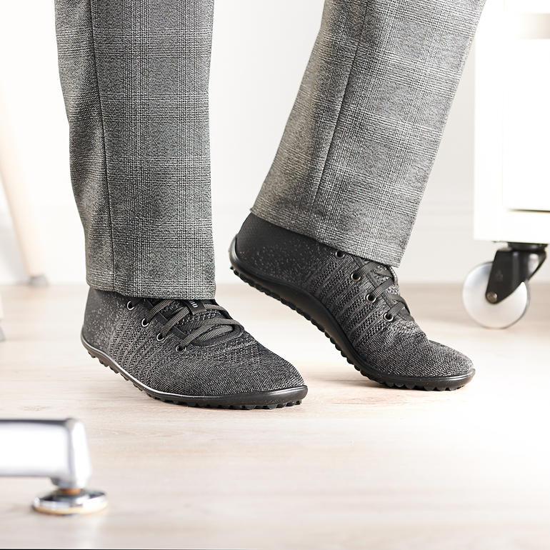 Homme portant des baskets noires Barfuß-leguano® Knit dans un bureau moderne.