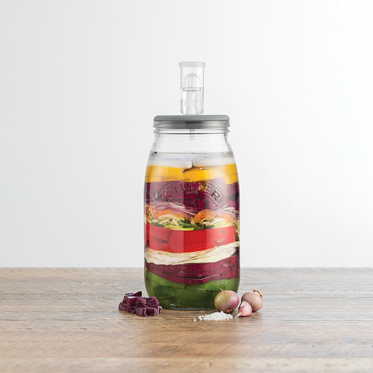 Grâce au barboteur intégré au couvercle hermétique, il ne se forme pas de surpression dans le bocal pour une fermentation parfaite de mets délicats. Bocal de fermentation avec évent, rempli de légumes colorés en couches.