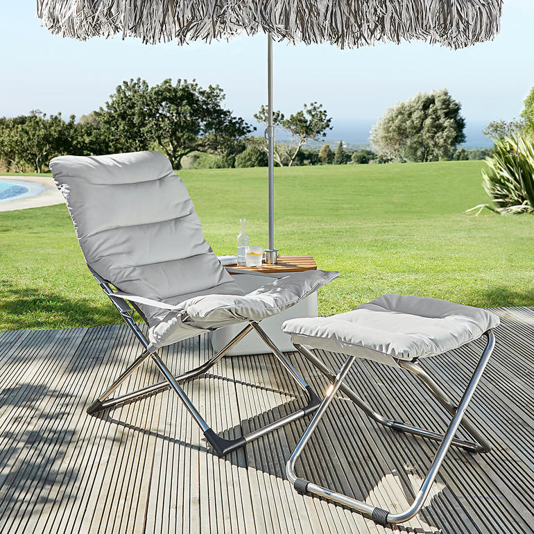 Fauteuil pliable Fiam et repose-pieds sur une terrasse avec parasol.